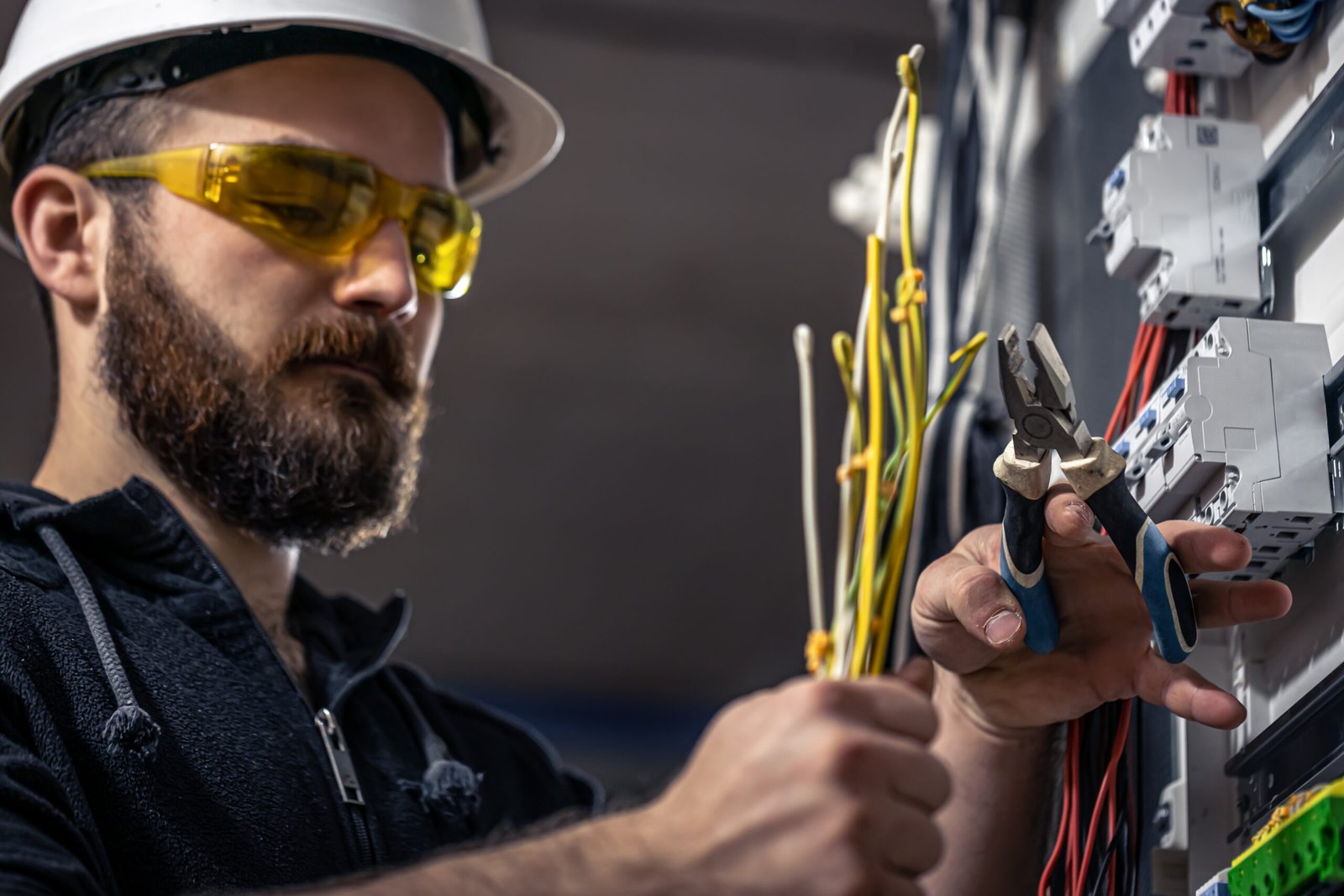 a male electrician works in a switchboard with an electrical connecting cable.